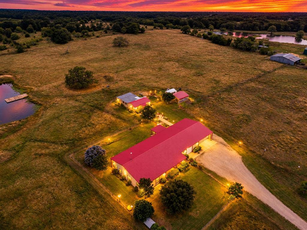 5801 County Road 4128, Scurry, TX 75158 Expansive property featuring a red-roofed primary structure, multiple outbuildings, and a pond with a dock