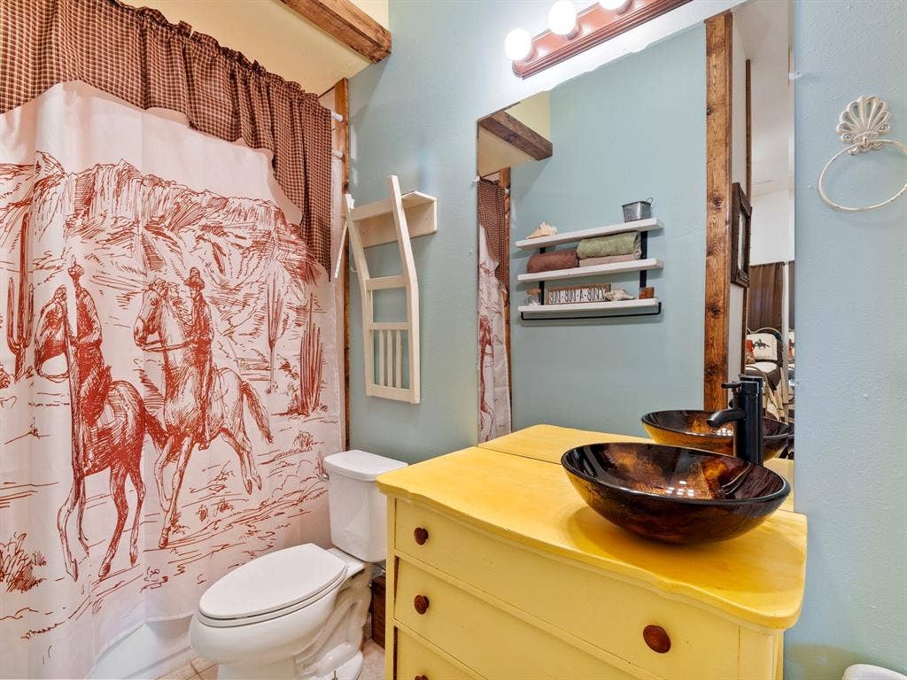 5801 County Road 4128, Scurry, TX 75158 Bathroom featuring a dark-toned glass vessel sink, matte black faucet, wall-mounted shelving, large rectangular mirror, and exposed wood ceiling beam