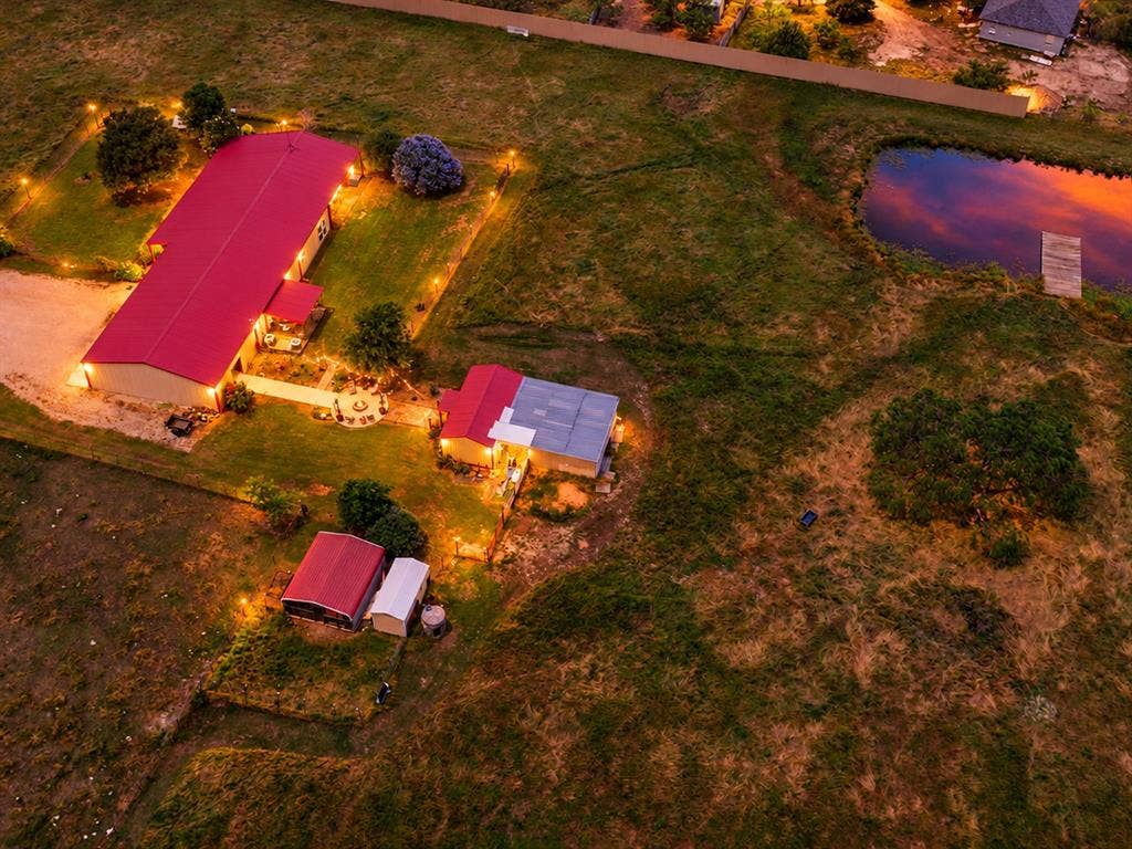 5801 County Road 4128, Scurry, TX 75158 Expansive property featuring multiple structures with red metal roofs, a private pond with a wooden dock, and extensive grounds