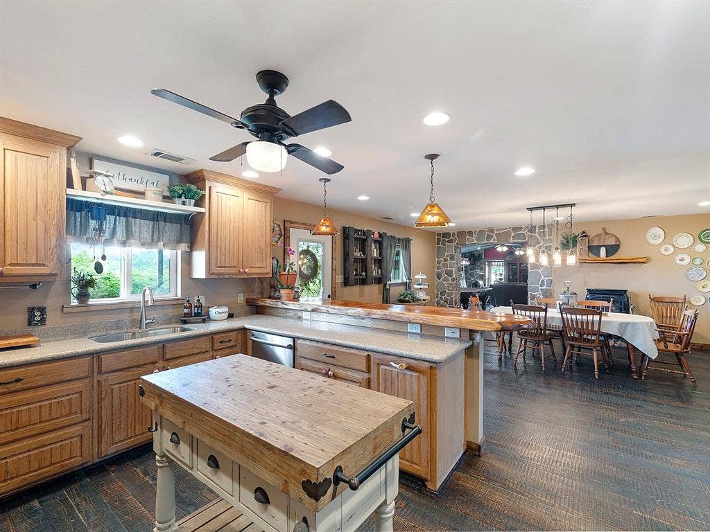 5801 County Road 4128, Scurry, TX 75158 Kitchen featuring wood cabinetry, solid-surface countertops, a built-in breakfast bar with live-edge wood top, wood-finish flooring, and natural stone fireplace surround