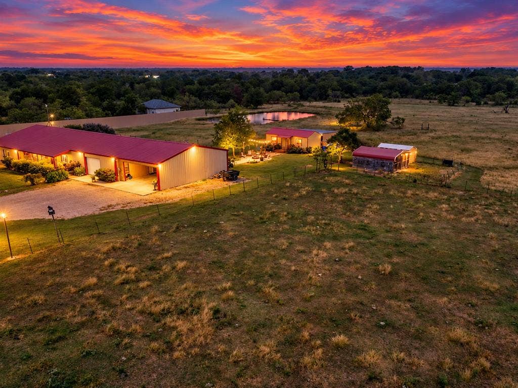 5801 County Road 4128, Scurry, TX 75158 Expansive property featuring multiple structures with red metal roofing, a large pond, and mature landscaping