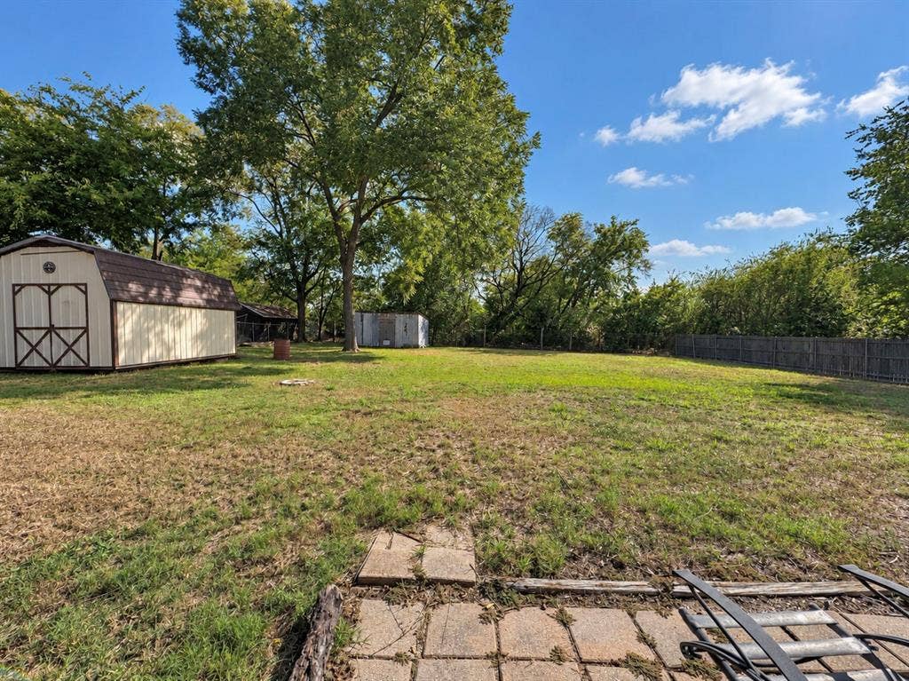 208 Olive Street, Lone Oak, TX 75453 Expansive green space featuring a large barn-style shed, additional storage shed, mature trees, and a wood privacy fence