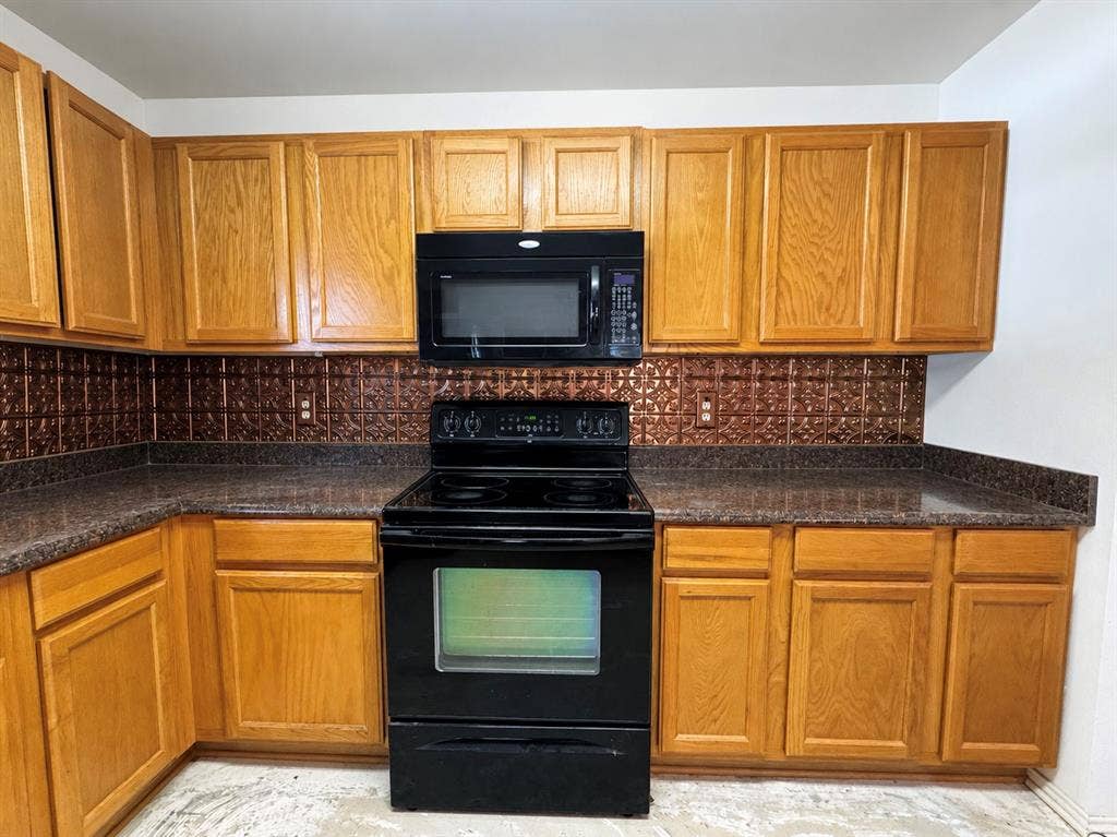 208 Olive Street, Lone Oak, TX 75453 Kitchen featuring wood-finish cabinetry, dark speckled countertops, a copper-toned pressed metal backsplash, and a black range with an over-the-range microwave