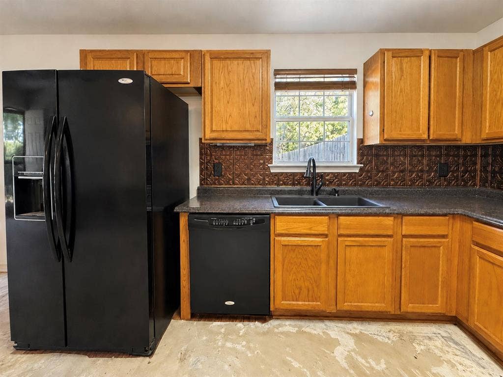 208 Olive Street, Lone Oak, TX 75453 L-shaped countertop with a dual basin sink, black appliances, wood cabinetry, and a textured backsplash