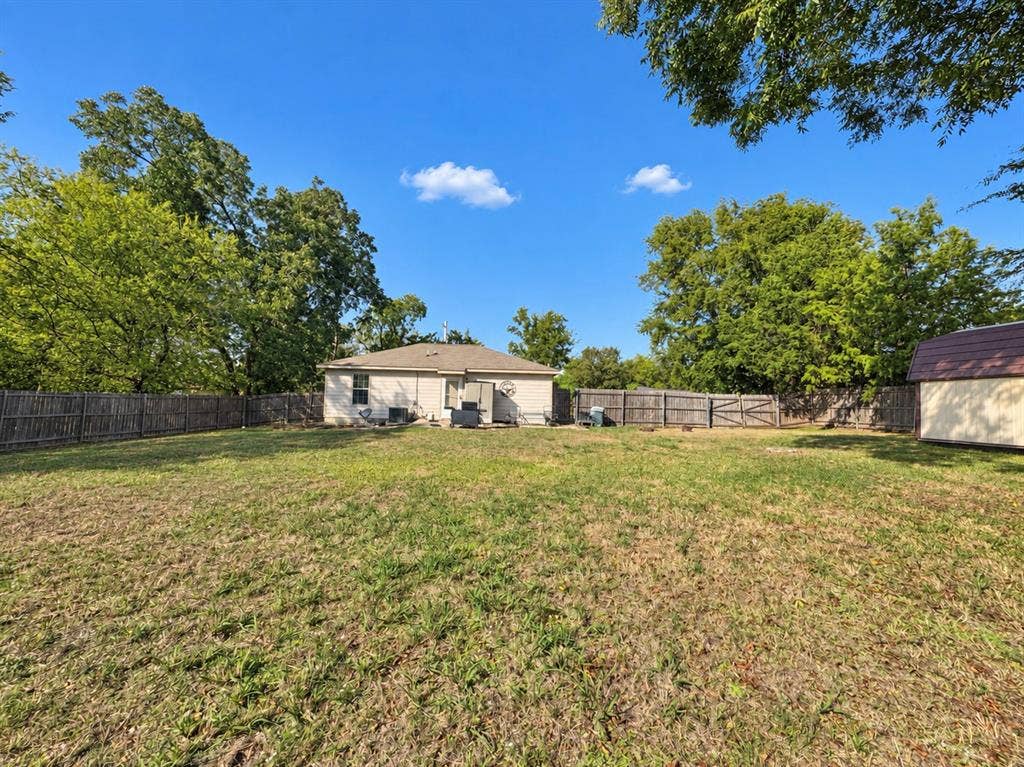 208 Olive Street, Lone Oak, TX 75453 Expansive rear yard with a perimeter wood fence, mature trees, and a detached shed
