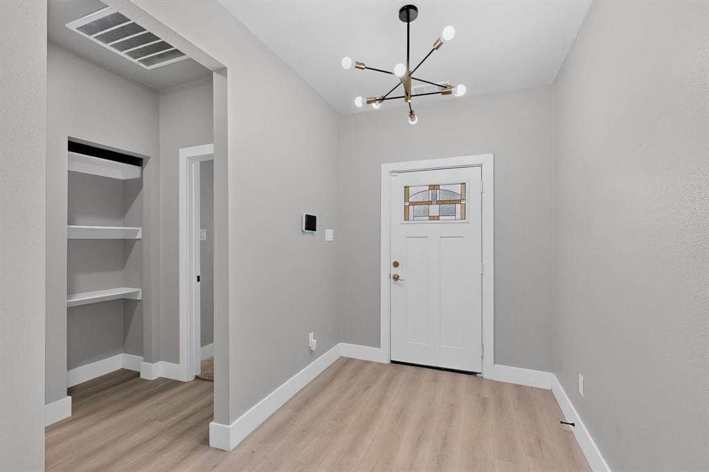 Entryway featuring wood-finish flooring, a contemporary multi-arm chandelier, an exterior door with a leaded glass insert, and built-in wall shelving