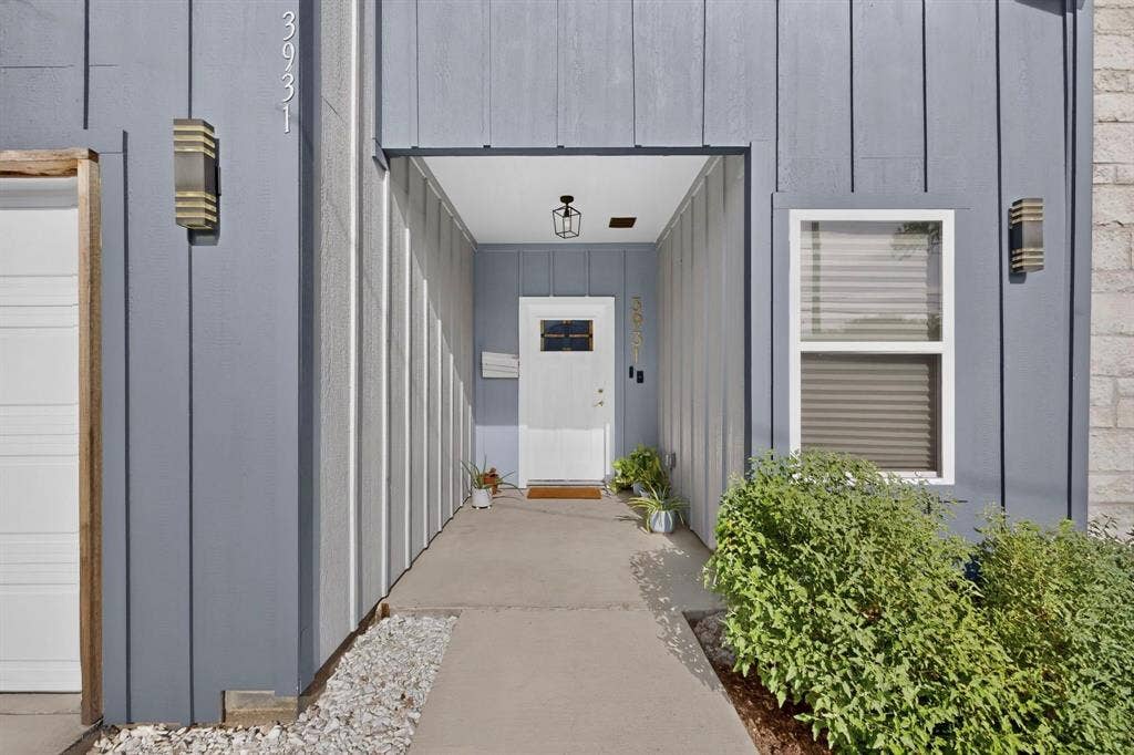 Covered entryway featuring vertical board-and-batten siding, a white front door with a window insert, concrete porch, and rectangular wall-mounted exterior lighting