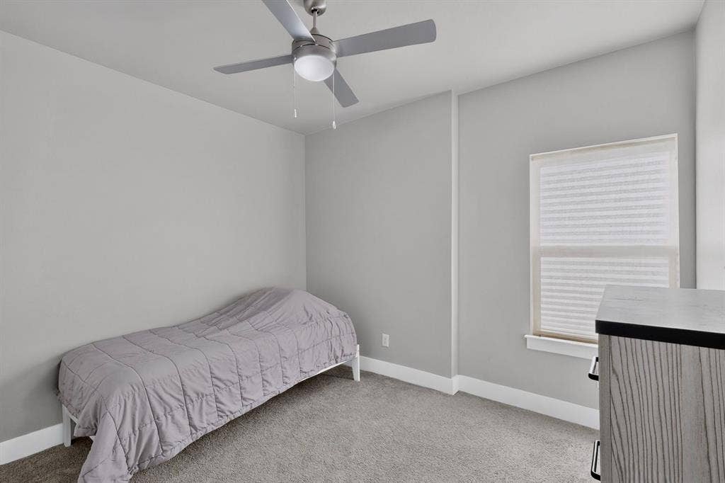 Neutral-toned room featuring neutral carpeting, a central ceiling fan with an integrated light fixture, and a window with a pleated shade