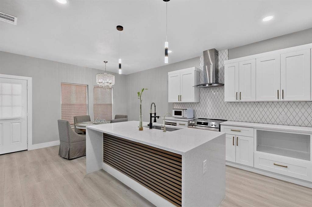 Kitchen featuring a center island with slatted wood detailing and a quartz countertop, white shaker-style cabinetry, a stainless steel range hood, diamond-pattern backsplash, and wood-finish flooring