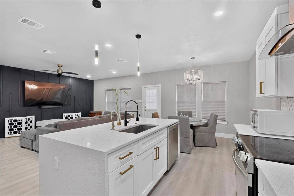 Kitchen featuring a quartz-topped center island with a stainless steel undermount sink, white cabinetry with metallic hardware, wood-finish flooring, recessed lighting, and a decorative accent wall