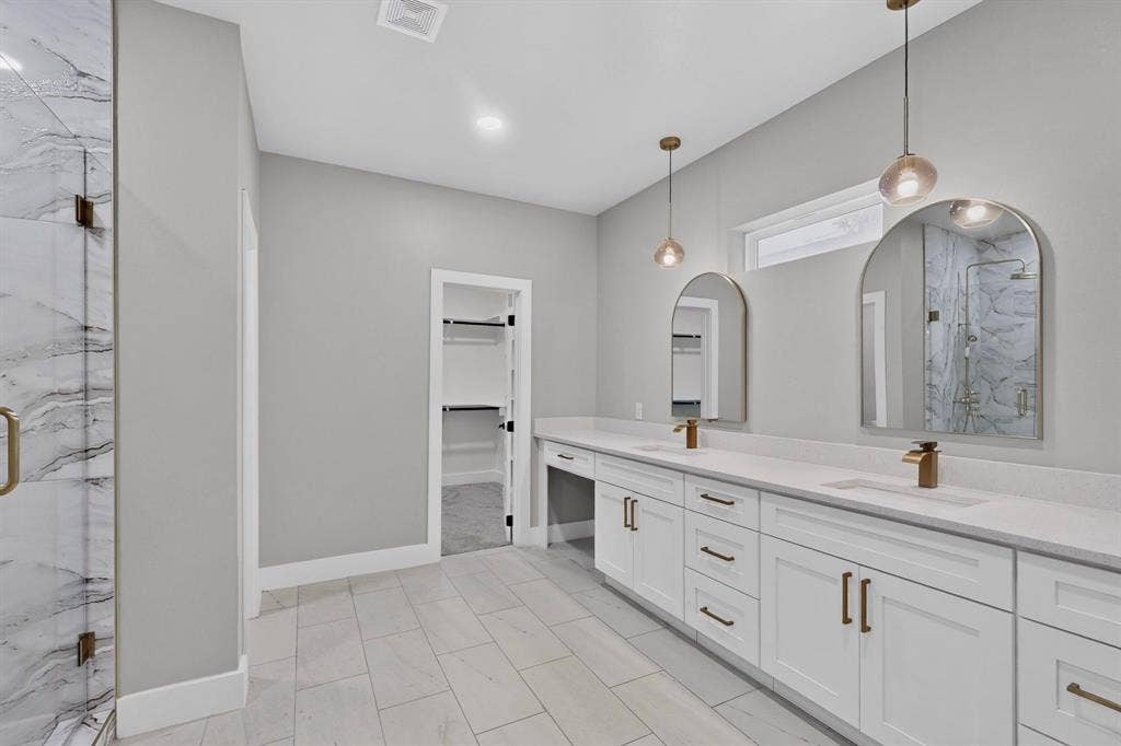 Double vanity featuring white cabinetry, quartz countertops, dual arched mirrors, metallic pendant lighting, and a walk-in closet