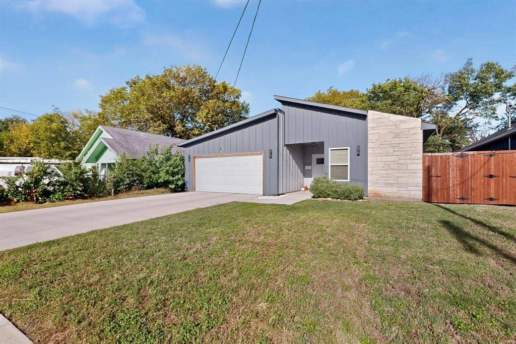 Modern exterior featuring vertical siding, a stone facade accent, mono-pitch roofline, two-car garage, and a wood privacy fence
