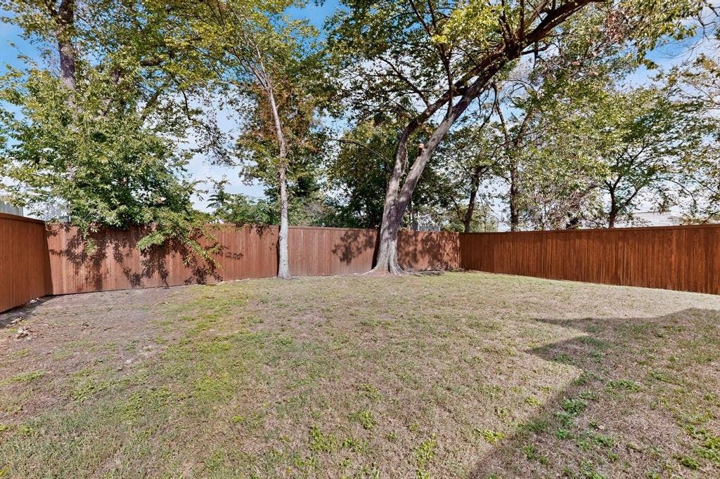 Fenced backyard featuring an expansive lawn and mature trees