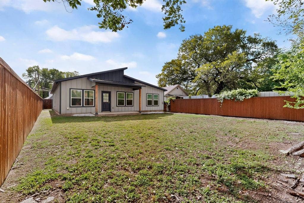 Exterior of a modern home featuring a shed roofline, vertical siding, a covered rear patio with a wood-accented support post, and a privacy-fenced backyard