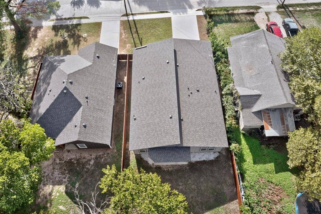 Aerial perspective featuring a central residence with a composition shingle roof, concrete driveway, and fenced rear grounds