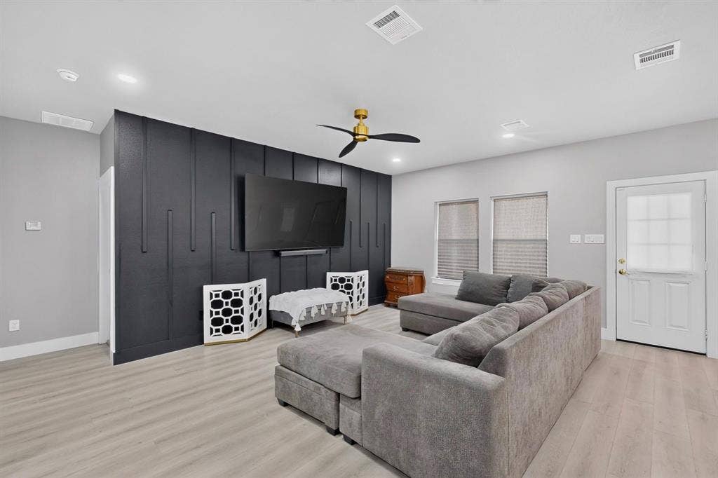 Living area featuring a black vertical slat accent wall, light-toned wood-finish flooring, and a ceiling fan with a metallic finish