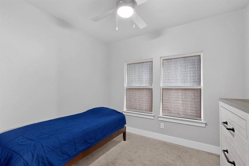 Neutral-toned interior featuring dual windows, wall-to-wall carpeting, and a ceiling-mounted light fixture with fan