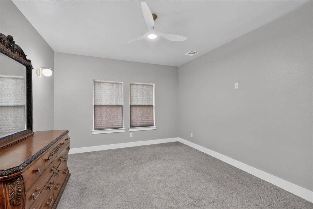 Neutral-toned interior featuring wall-to-wall carpeting, dual windows, and a ceiling-mounted fan with integrated lighting