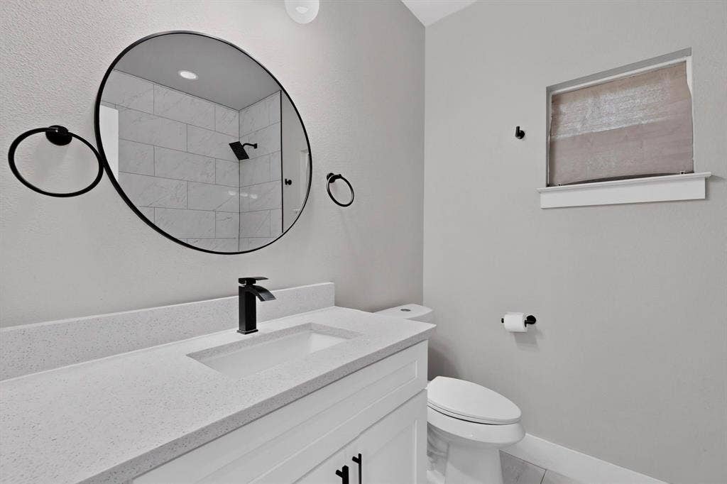 Modern vanity featuring a stone-composite countertop, rectangular undermount sink, matte black faucet, and circular wall-mounted mirror