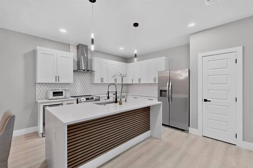 Kitchen featuring white shaker-style cabinetry, a central island with wood-slat detailing and stone countertop, stainless steel appliances, a geometric tile backsplash, and recessed ceiling lighting