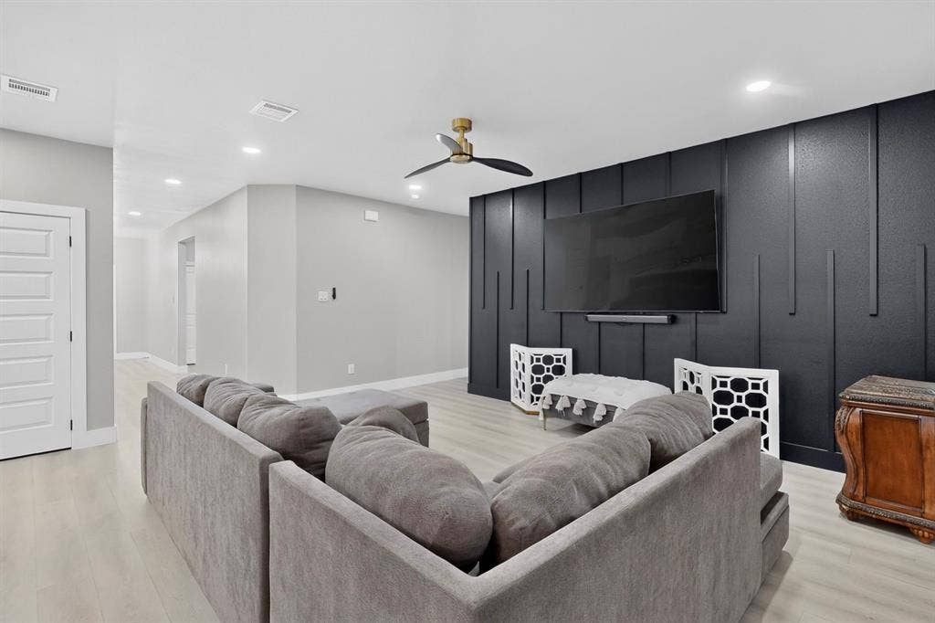 Living area featuring a black vertical slat accent wall, wood-finish flooring, recessed lighting, and a multi-blade ceiling fan