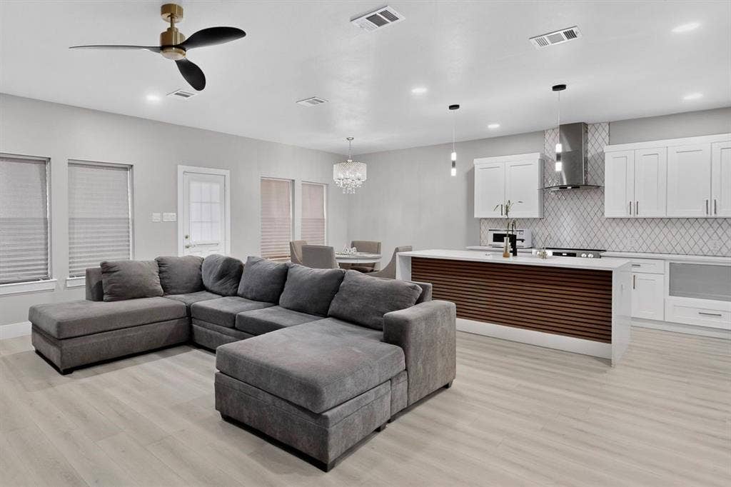 Open-concept kitchen featuring white shaker-style cabinetry, a slatted wood-accented island, stone-patterned backsplash, recessed lighting, and wood-finish flooring