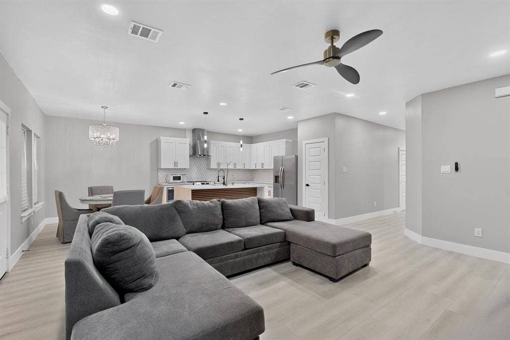 Open-concept layout featuring wood-finish flooring, recessed lighting, a modern ceiling fan, and a kitchen equipped with white shaker-style cabinetry, stainless steel appliances, and a central island with a wood-accented base