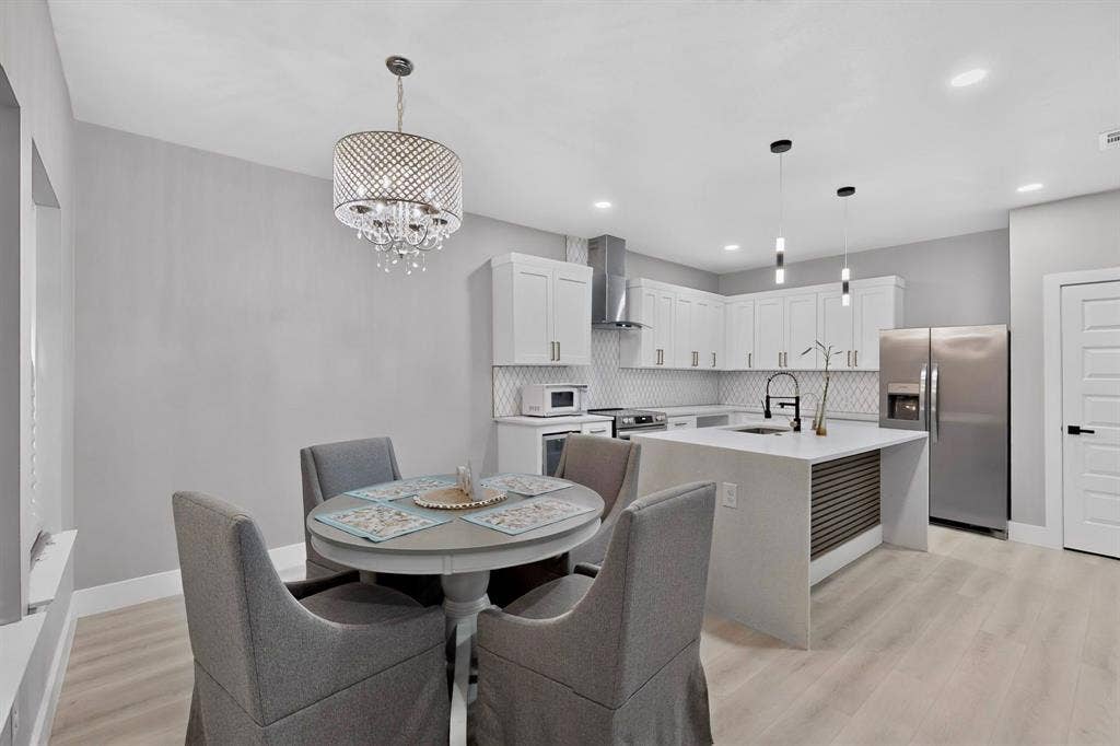 Kitchen featuring white cabinetry, an island with stone-finish countertop, stainless steel appliances, geometric tile backsplash, and wood-finish flooring