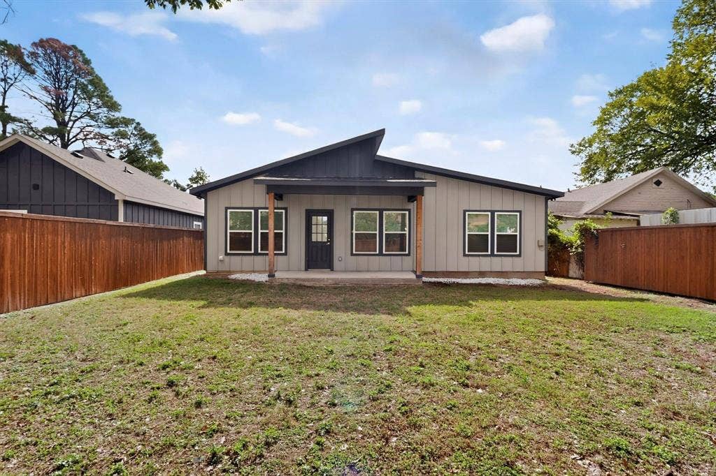 Rear exterior featuring a shed-style roofline, board-and-batten siding, a covered porch with timber support posts, and a full-height wood privacy fence