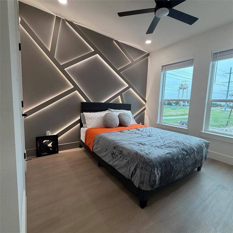 Accent wall featuring geometric paneling with integrated LED lighting, wood-finish flooring, recessed ceiling lighting, and a multi-blade matte black ceiling fan