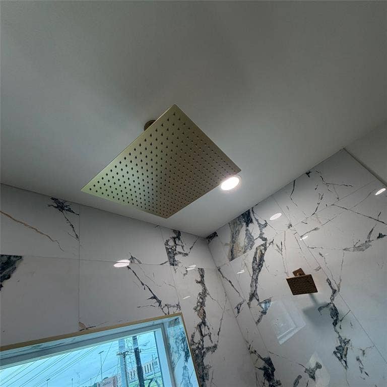 Large square rainfall shower head with brass-tone finish, wall-mounted matching handheld shower fixture, and large-format tile wall cladding featuring veined patterns