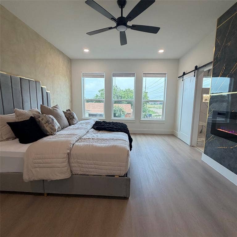 Floor-to-ceiling accent wall with integrated fireplace, wood-finish flooring, matte black ceiling fan, recessed lighting, and sliding barn door