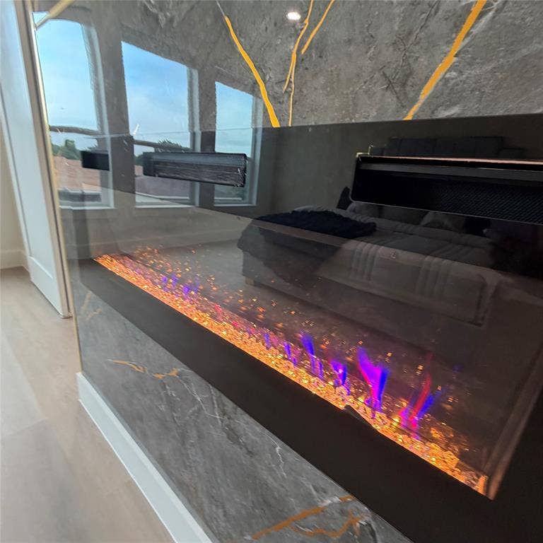 Linear wall-mounted electric fireplace featuring a dark glass surround, integrated crystal ember bed, and floor-to-ceiling gray veined stone cladding
