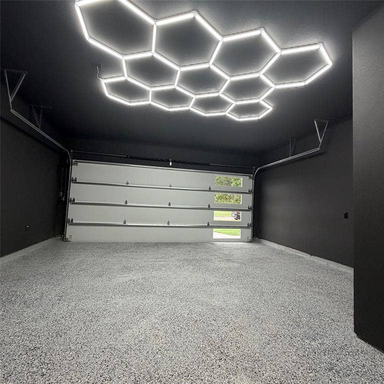 Garage interior featuring a custom honeycomb LED ceiling light array, high-contrast matte walls, speckled epoxy-coated flooring, and an insulated garage door with horizontal rectangular glass inserts
