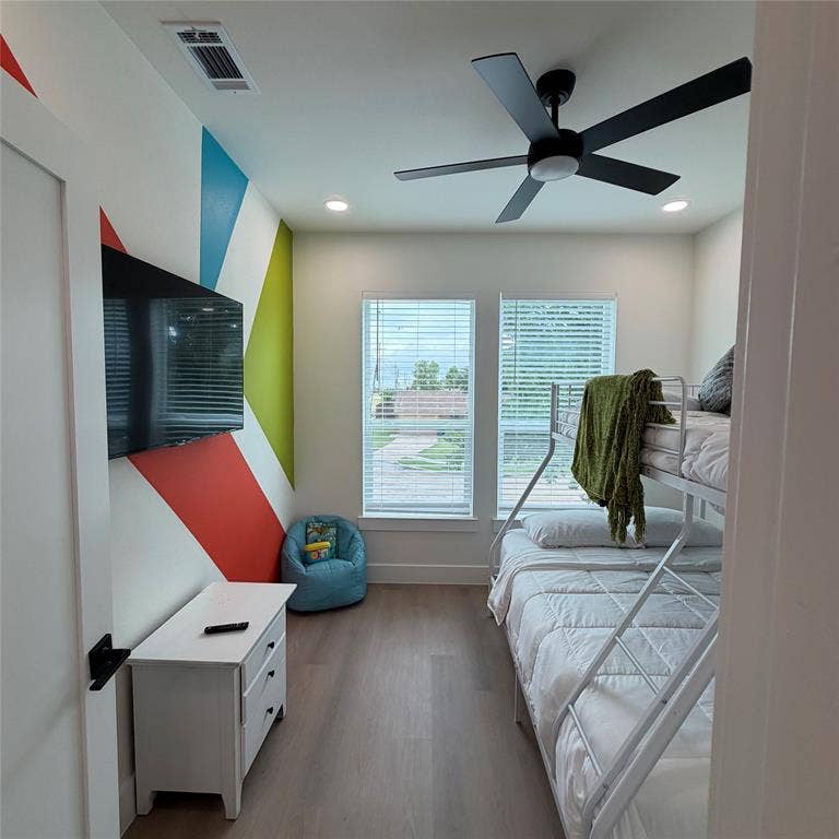 Wood-finish flooring, matte black ceiling fan with integrated lighting, dual windows with blinds, and recessed lighting