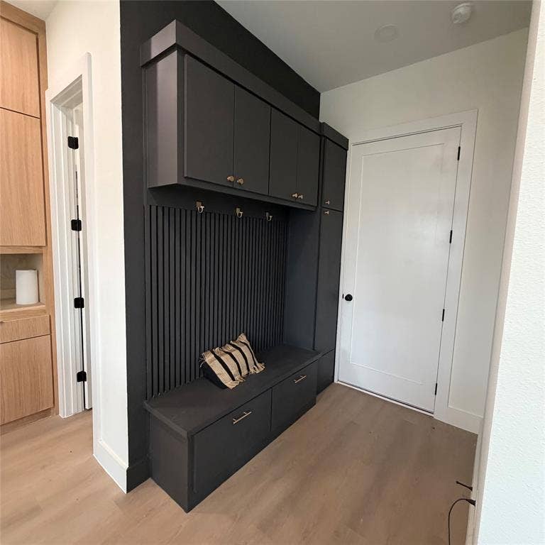 Built-in dark gray cabinetry featuring upper storage, integrated bench seating with lower drawer storage, metallic hardware, and vertical slat wall detailing, set against wood-finish flooring