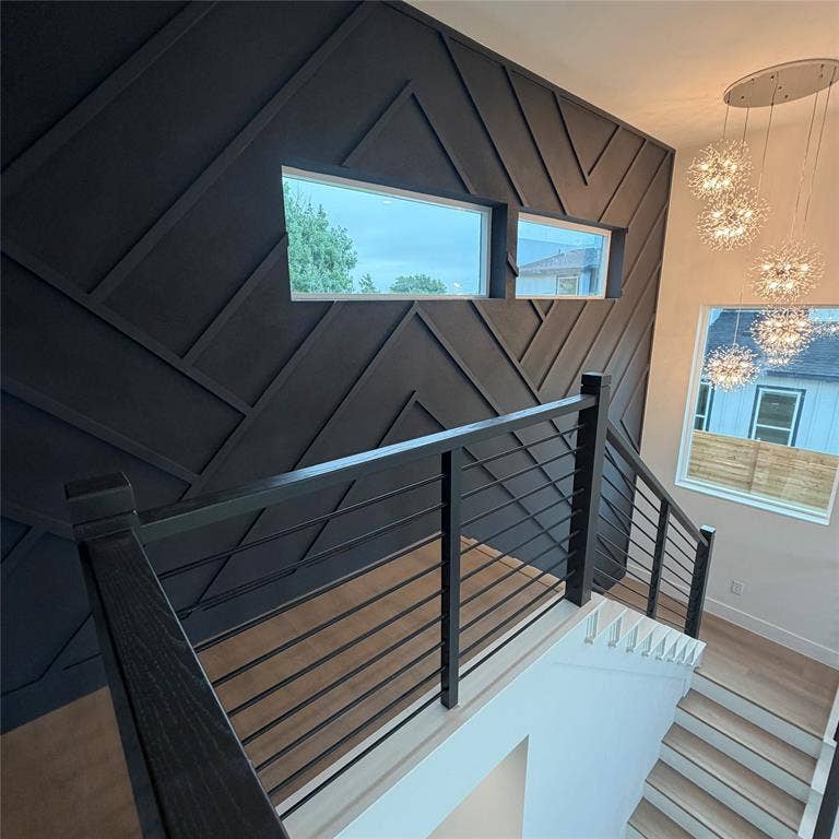 Interior wall featuring dark-toned geometric millwork, horizontal windows, light wood-finish flooring, cable-rail staircase, and multi-pendant cluster lighting