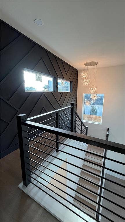 Staircase featuring a geometric dark-toned accent wall, cable railing system, wood-finish treads, and multi-tier pendant lighting