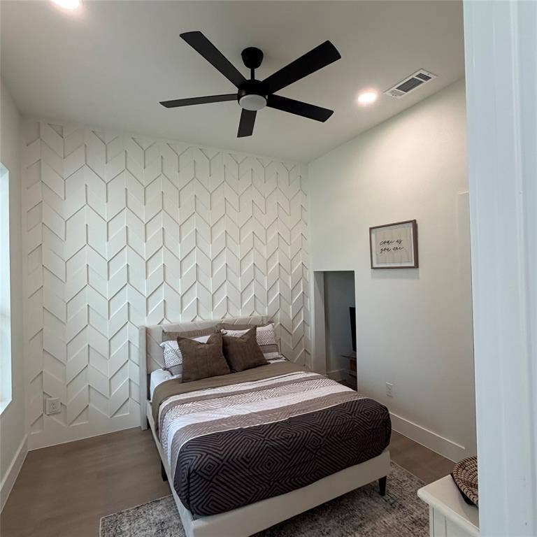 Geometric custom wood wall detailing, wood-finish flooring, and a matte black ceiling fan