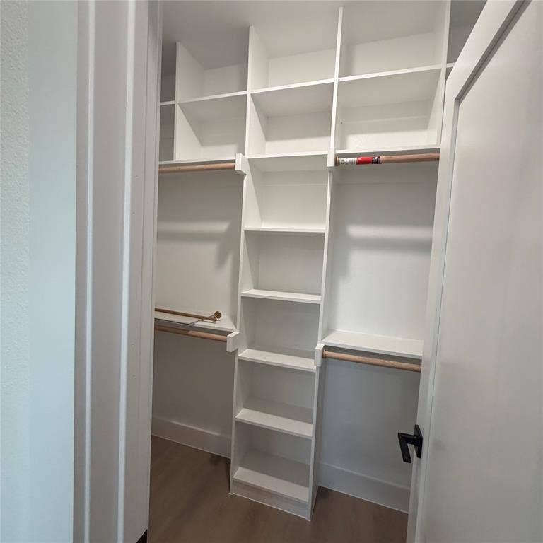 Custom closet featuring white built-in shelving, wood-finish hanging rods, and wood-finish flooring
