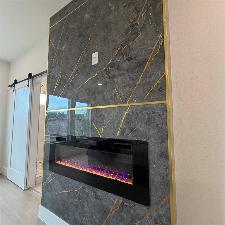 Floor-to-ceiling fireplace surround featuring dark stone-finish panels with gold-tone metal inlay, a built-in linear electric fireplace, and a white interior sliding barn door