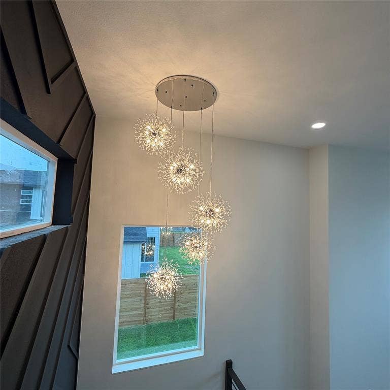 Multi-tiered starburst chandelier featuring five spherical fixtures, dark-toned geometric accent wall paneling, and rectangular windows