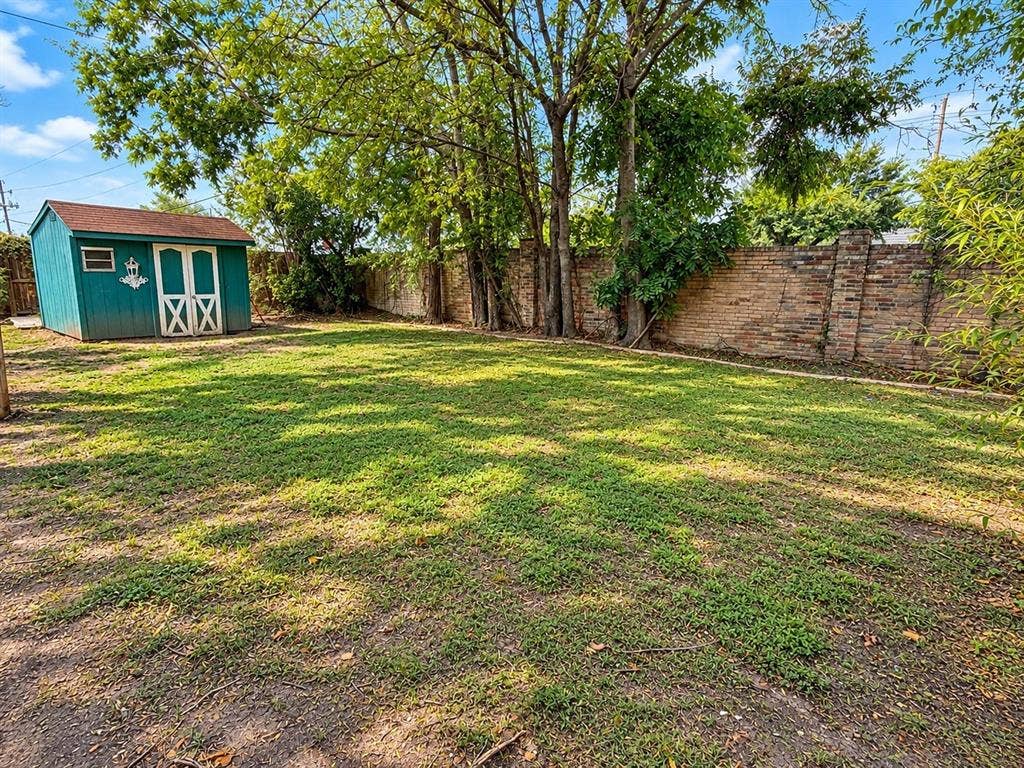 1444 Marlene Place, DeSoto, TX 75115 Expansive grassy yard with mature trees, a brick perimeter wall, and a separate storage shed with double doors