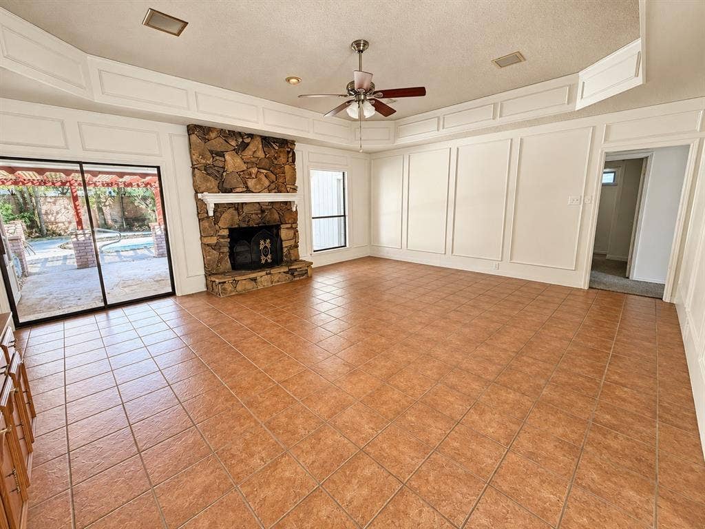 1444 Marlene Place, DeSoto, TX 75115 Stone fireplace, tile flooring, decorative wall molding, ceiling fan, and sliding glass doors to the exterior