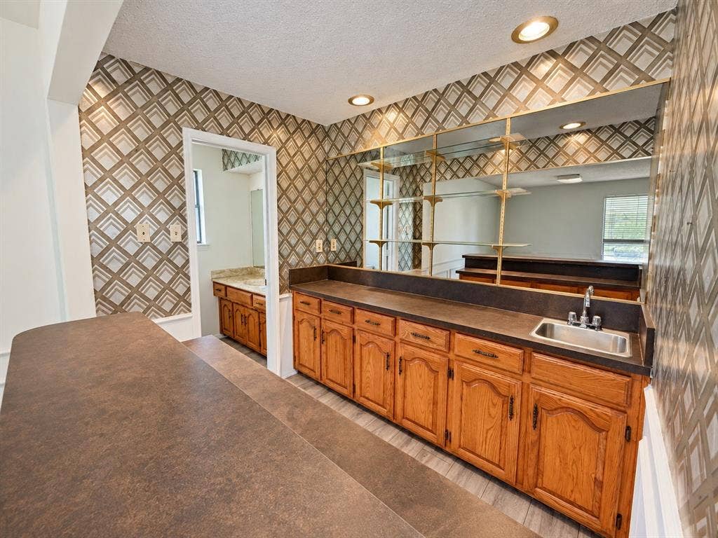 1444 Marlene Place, DeSoto, TX 75115 Built-in cabinetry with a stainless steel sink, large mirrored wall with shelving, recessed lighting, and patterned wall covering