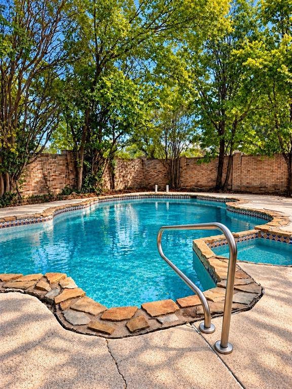 1444 Marlene Place, DeSoto, TX 75115 Irregularly shaped swimming pool featuring a stone coping, integrated spa, and stainless steel grab rail, surrounded by a concrete deck and mature trees