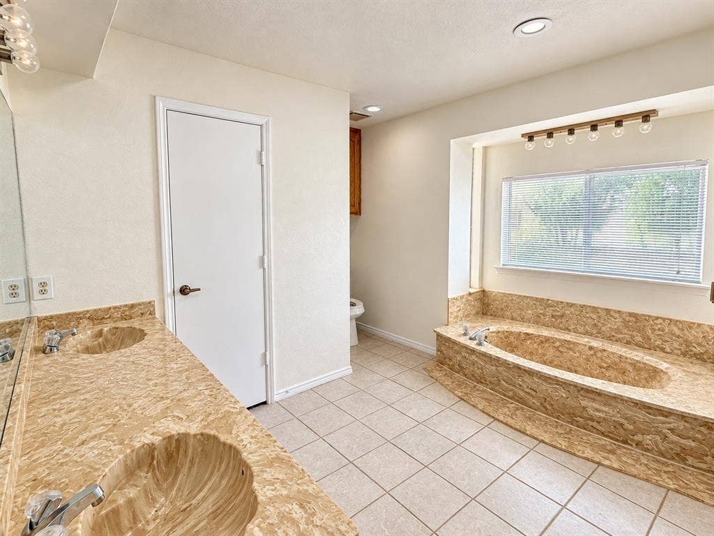 1444 Marlene Place, DeSoto, TX 75115 Dual vanity with integrated shell-shaped sinks, tiled flooring, and a built-in soaking tub with a window