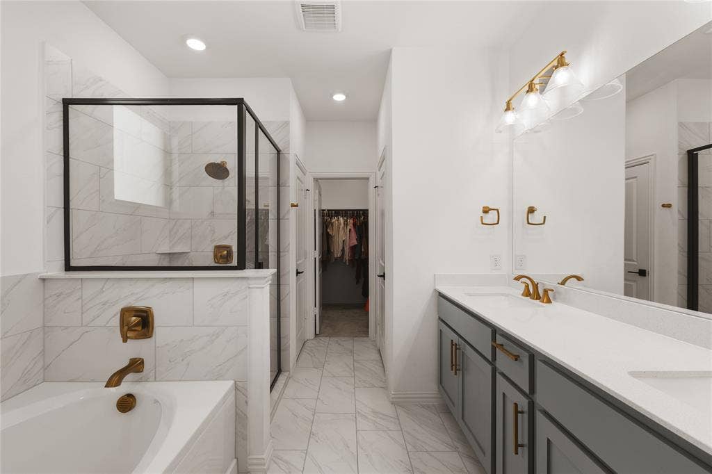 1456 Martingale Lane, Forney, TX 75126 Bathroom featuring a dual-sink vanity with solid-surface countertops, walk-in shower with matte black framing, soaking tub, and stone-finish tile flooring