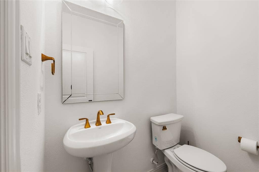 1456 Martingale Lane, Forney, TX 75126 Wall-mounted beveled mirror, white pedestal sink with brass-toned widespread faucet, and matching brass-toned hardware
