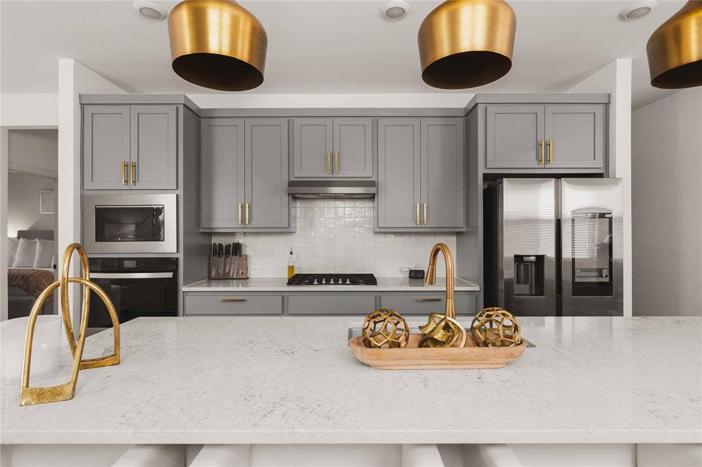 1456 Martingale Lane, Forney, TX 75126 Kitchen featuring gray shaker-style cabinetry, a stone-finish island countertop, brass-tone hardware, pendant lighting, and stainless steel appliances